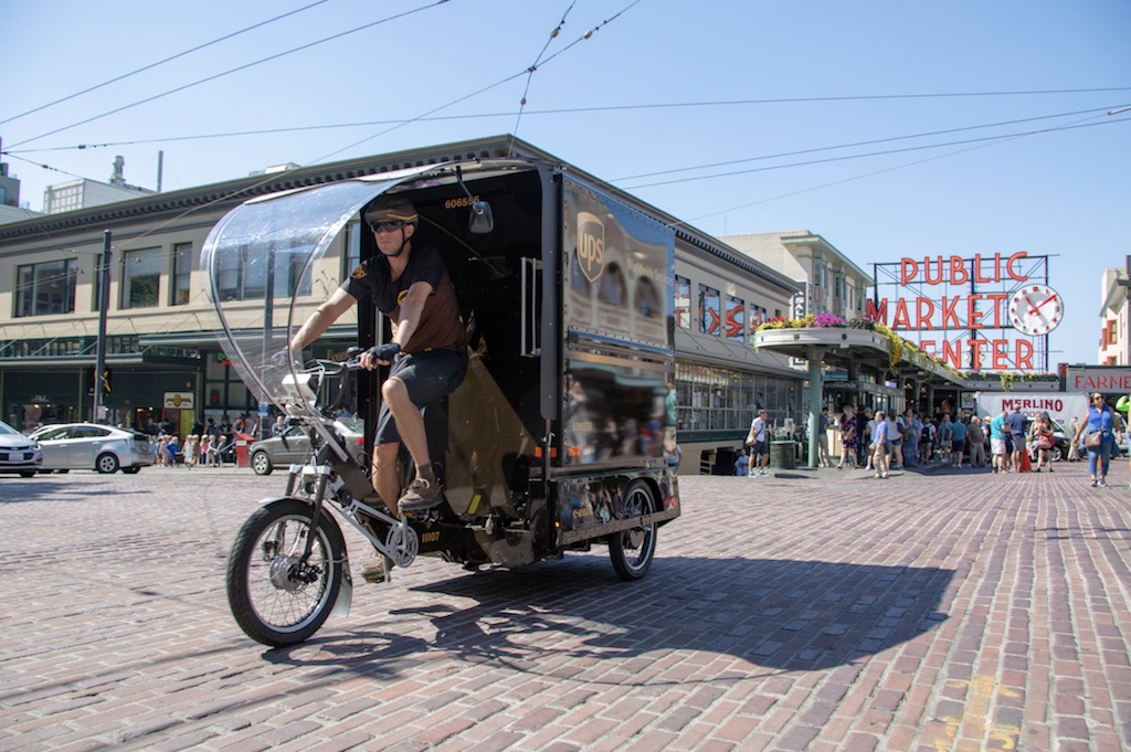 Cyclist pedaling a three-wheeled cargo delivery bike.