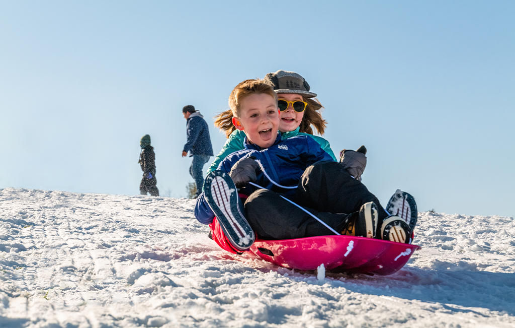 Two kids sledding down a snow-covered hill