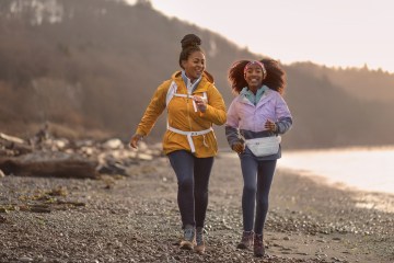 An image of two friends running on a rocky beach at sunset