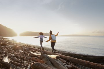 Two people walking on logs on a beach with sun setting.