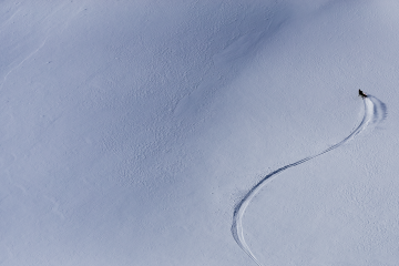 Michelle Parker captured from an aerial camera skiing down a mountain. She is a tiny bright spot in a sea of white.