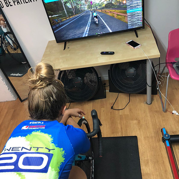 Picture show back a rider on bike as she faces a TV screen during a virtual cycling race.