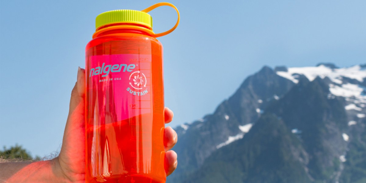A hand holds a Nalgene water bottle with snowcapped peaks in the distance