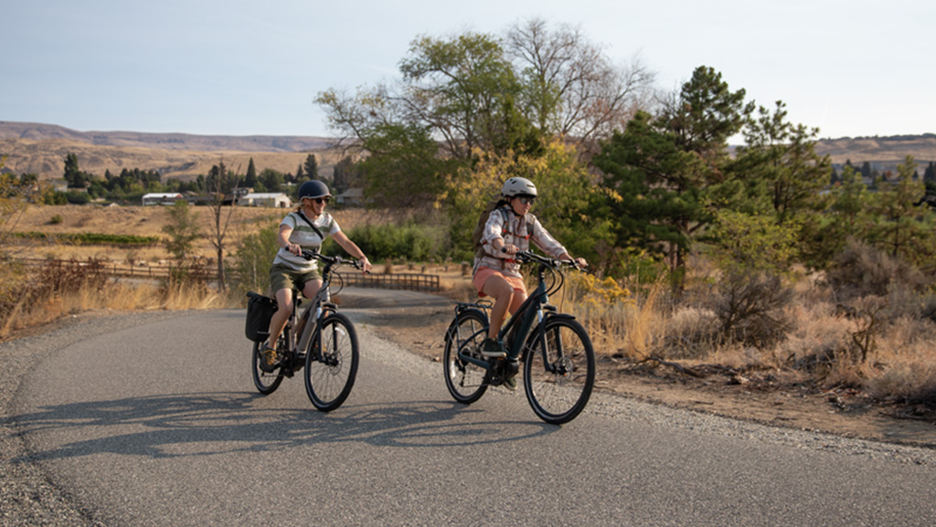 Two people riding electric bikes on a path.