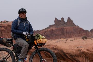 Person standing on bike in desert setting.