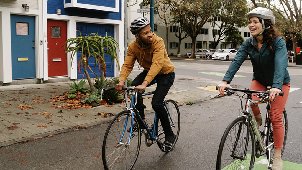 Two cyclists riding next to each other in an urban neighborhood.