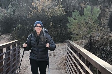 Woman hiker wearing sunglasses and using trekking poles as she crosses a wooden boardwalk bridge