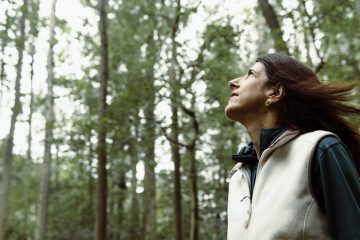 Florence Williams stands in front of trees looking up at the sky.