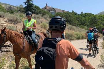 Person on a bike waits as person riding a horses passes on the trail