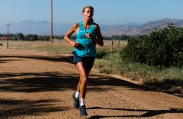 Leah is running in a blue shirt on a dirt road with a blue sky behind her.