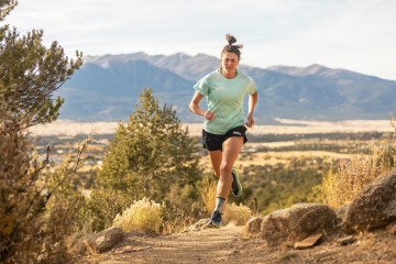 Gina Lucrezi running on a trail. She's wearing a teal shirt and black shorts.