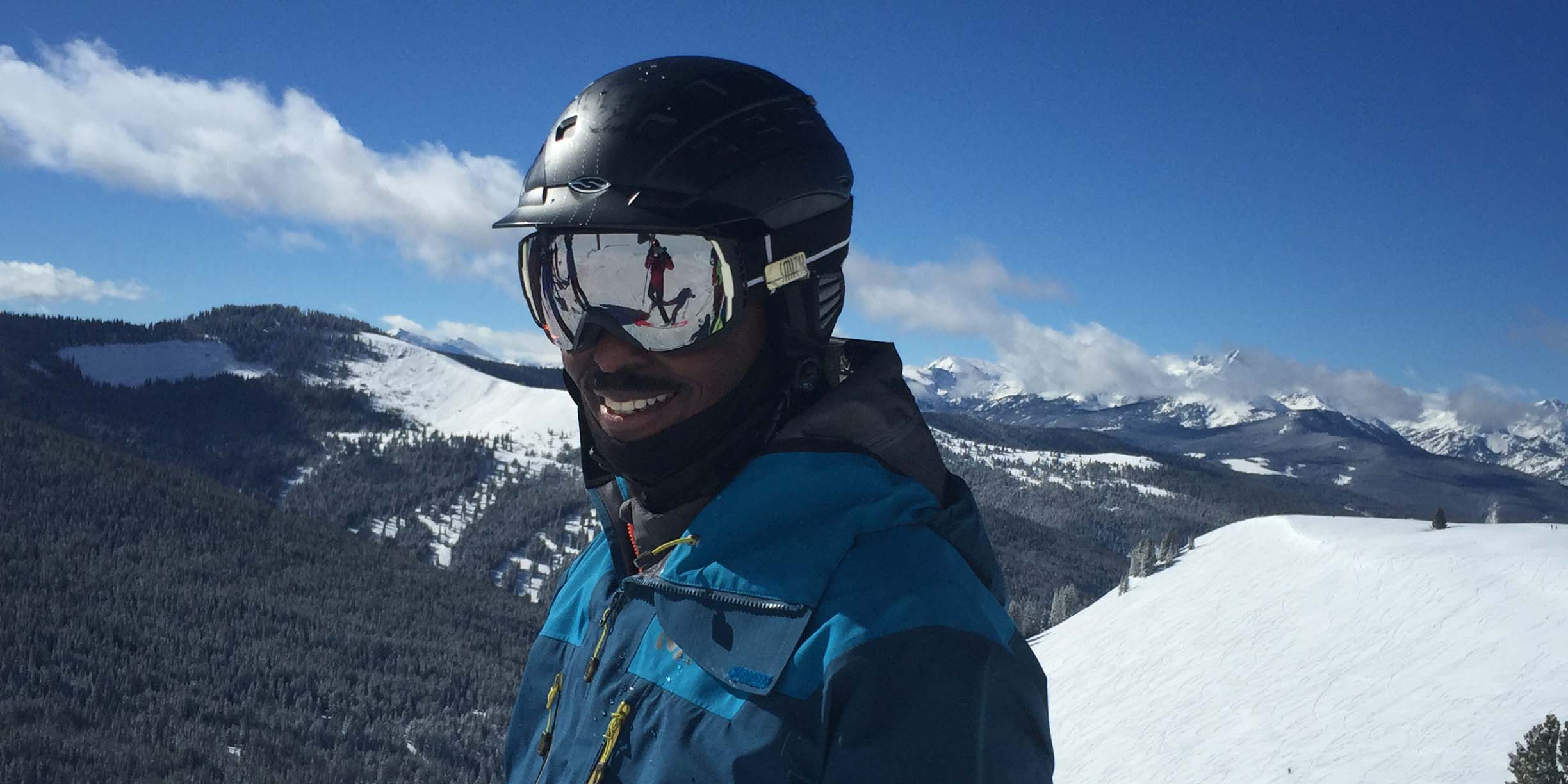 Mike Carey in helmet and goggles in front of snowy backdrop.