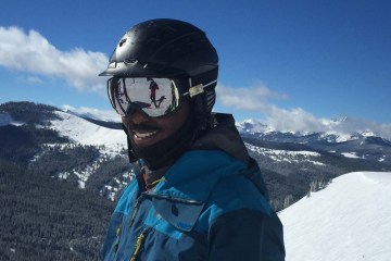 Mike Carey in helmet and goggles in front of snowy backdrop.