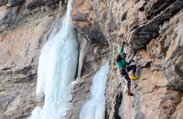 Climber Eddie Taylor is in the foreground rock climbing and there's a frozen waterfall in the background.