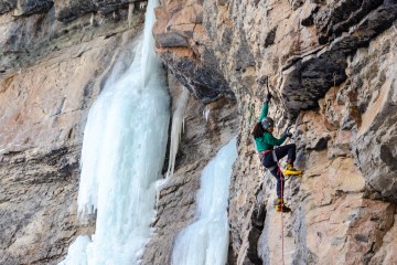 Climber Eddie Taylor is in the foreground rock climbing and there's a frozen waterfall in the background.