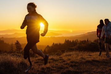 Nicole Ver Kuilen is running with two friends on a trail with a golden sunset behind her.