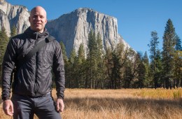 Davis Smith, founder of Cotopaxi, stands in front of a mountain wearing a black puffy jacket and smiling at the camera.