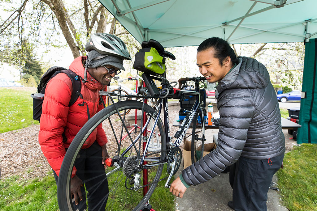 A cyclist looks on while another person tunes up a bike.