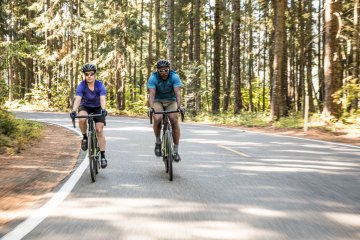 Two people biking on an empty road surrounded by trees