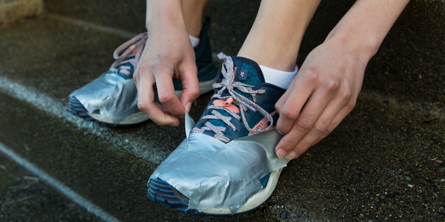 A person puts duct tape around the top of their running shoe, avoiding the laces.