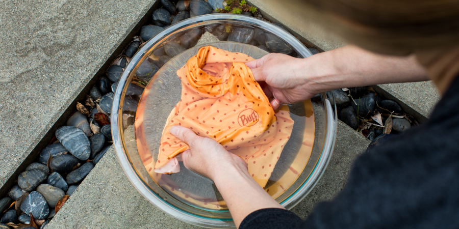 A person soaks an orange neck gaiter in a bowl of cold water.