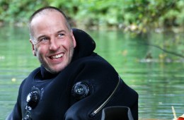 Rick Stanton is in the water wearing a diving suit and smiling at the camera.