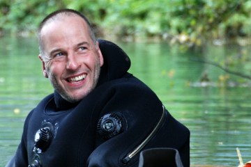 Rick Stanton is in the water wearing a diving suit and smiling at the camera.