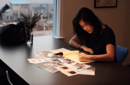 Gloria Hwang is leaning over a table writing on a yellow tablet.