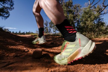 Person running in a pair neon-yellow-and-orange of adidas Agravic Flow 2 trail running shoes on a dirt trail.