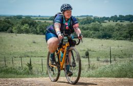 Marley Blonksy is riding a bike on a dirt path with a green field behind her.