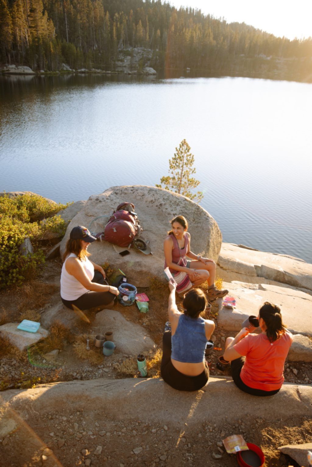 A group of friends isit on a rocky outcropping over a body of water, sharing a meal.