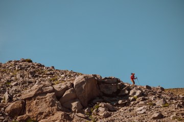 A man wearing a red jacket and using trekking poles runs down rocky mountain terrain in Washington State