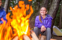 Two young people sit smiling around a camp fire
