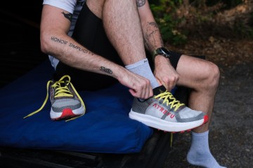 A person with an "Honor Simplicity" tattoo on their arm puts on a pair of the Atreyu Base Trail running shoes.