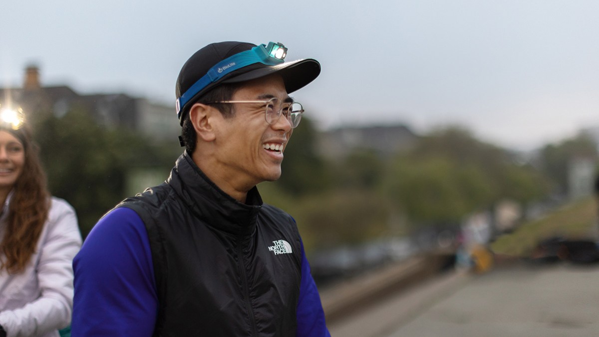 A smiling runner wears a blue headlamp on his baseball cap.