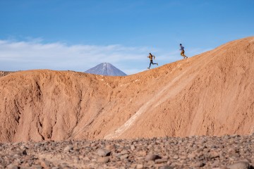 Two runners traversing a mountain ridge, wearing clothing from the Janji Runterra Bio collection