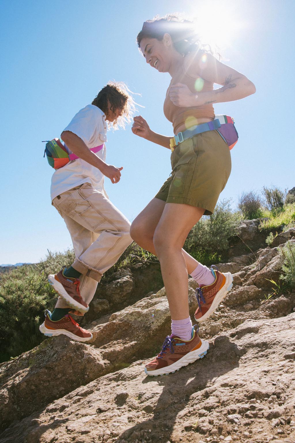 Two people in running shoes hike on rocky terrain.