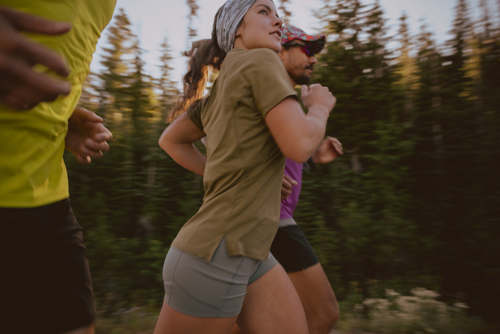 A woman runs with friends in a grey Buff Coolnet UV Multifunctional Neckwear and REI Co-op Swiftland Running T-Shirt in olive.