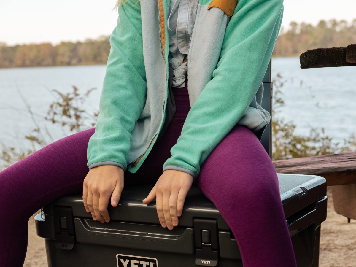 A woman sits on a black YETI cooler.
