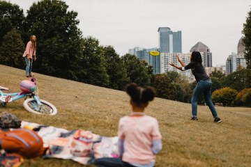 A group of people spend time at the park. Two of the people are throwing a frisbee.