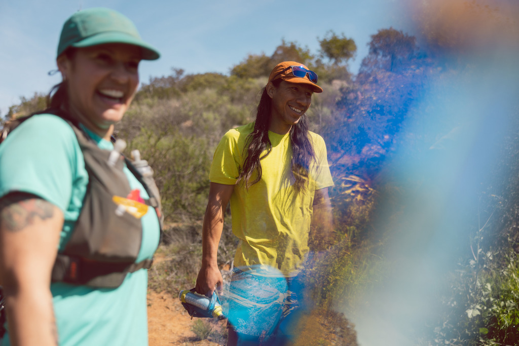 Two runners smiling, wearing REI Co-op On The Trail hats in blue and orange