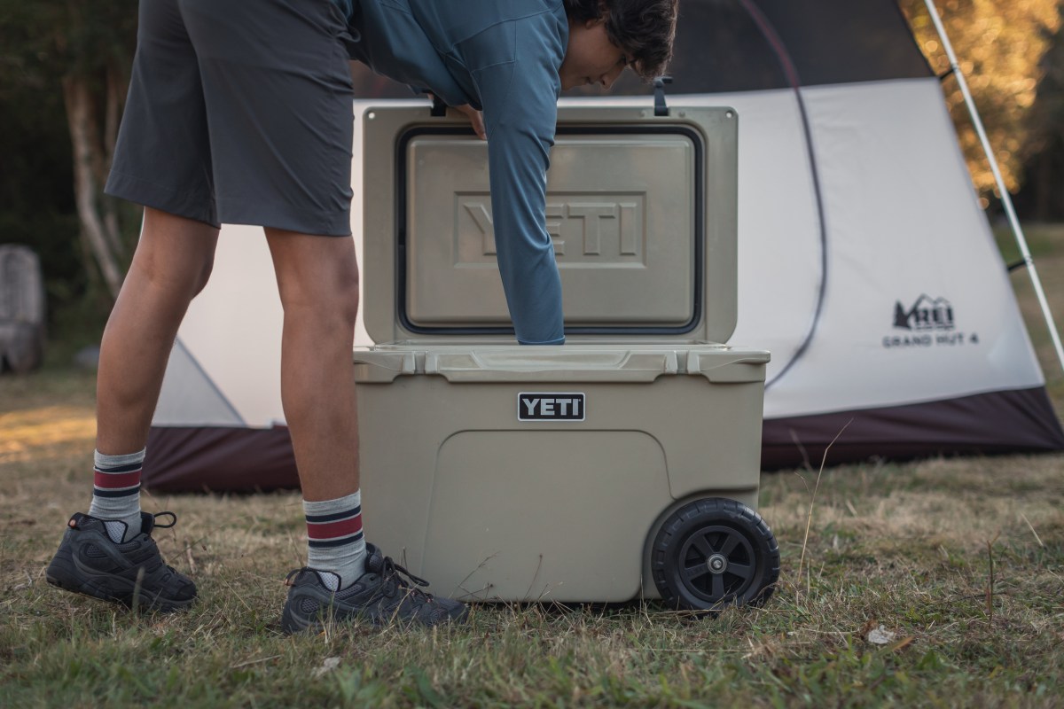 A young guy reaches into an open a YETI hardsided cooler at camp.