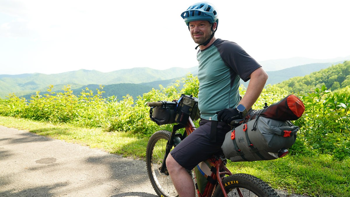 A person waits on a bike at an overlook with views of the mountains in the background.