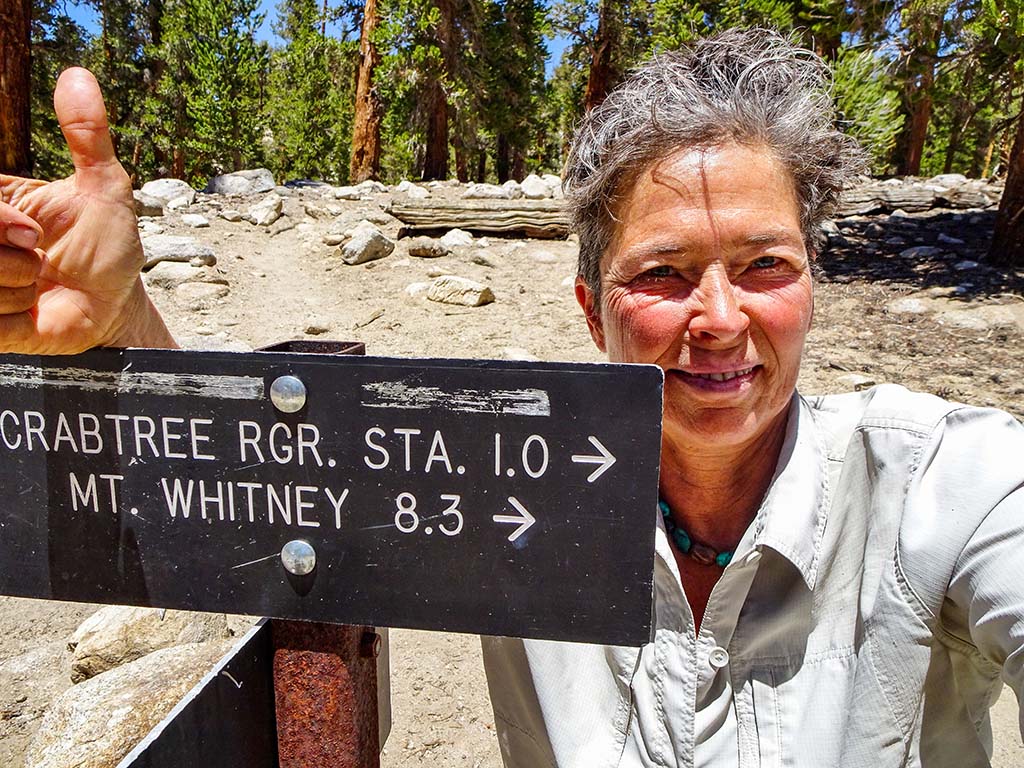 A person takes a selfie near a trail marker