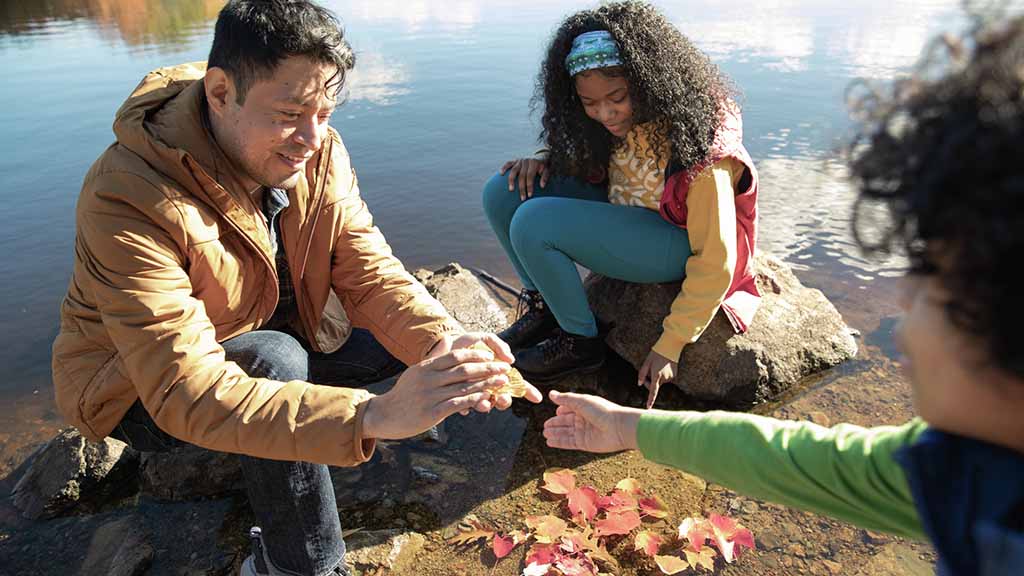 An adult and two children sit outside examining a fall leaf together