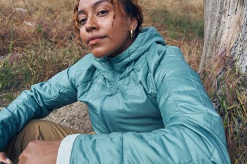 A person wearing a Circaloft jacket by The North Face sitting in a field