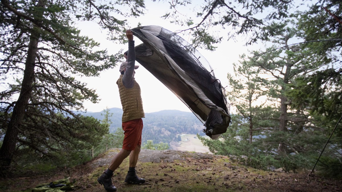 A man shakes out his tent at his campsite.