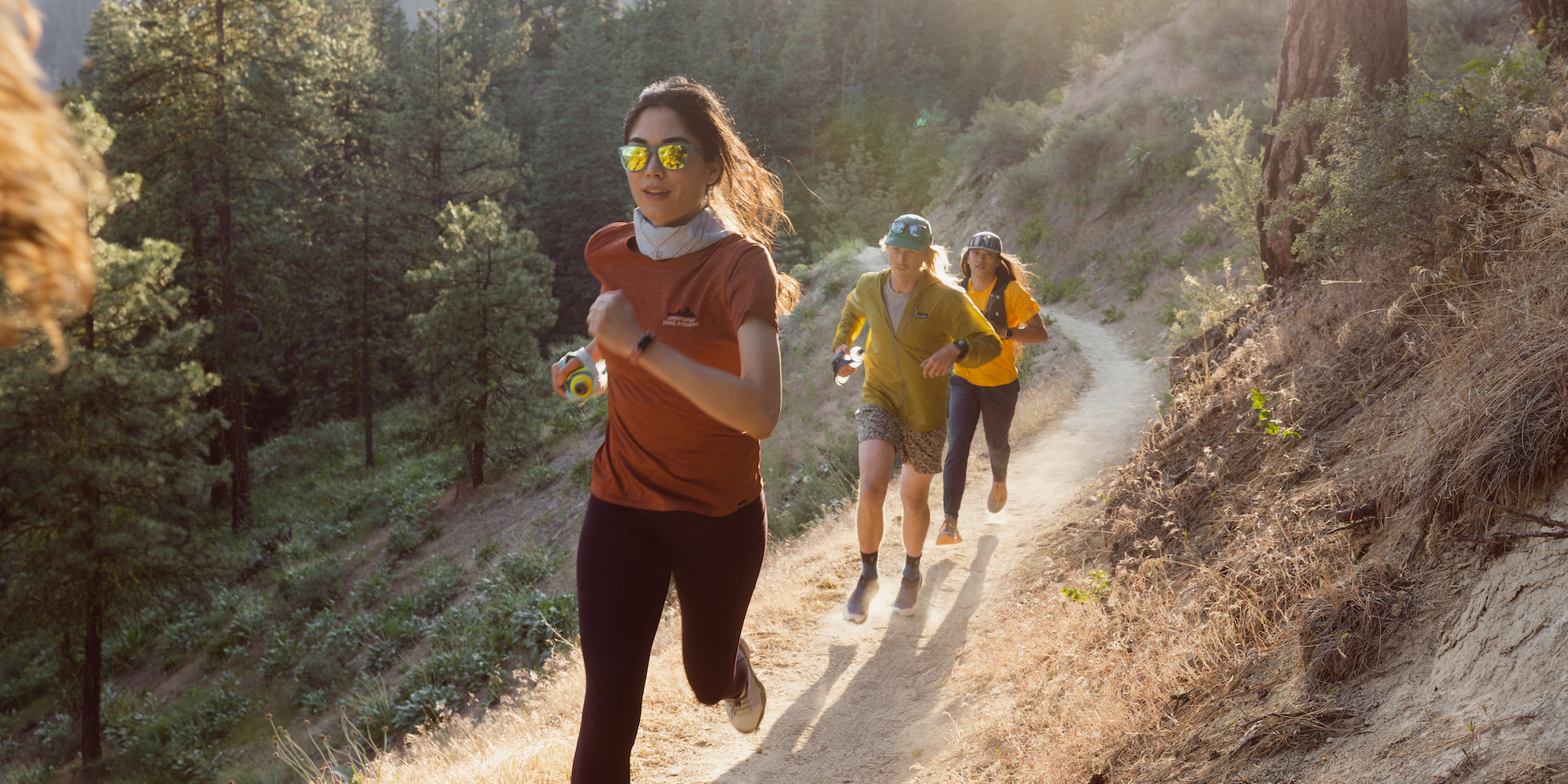 Three people running on a mountain trail, as if towards the camera.