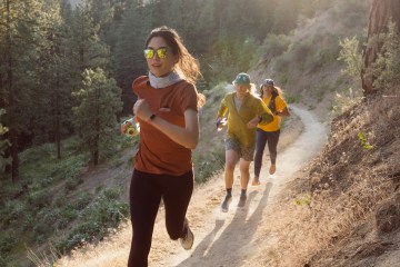 Three people running on a mountain trail, as if towards the camera.