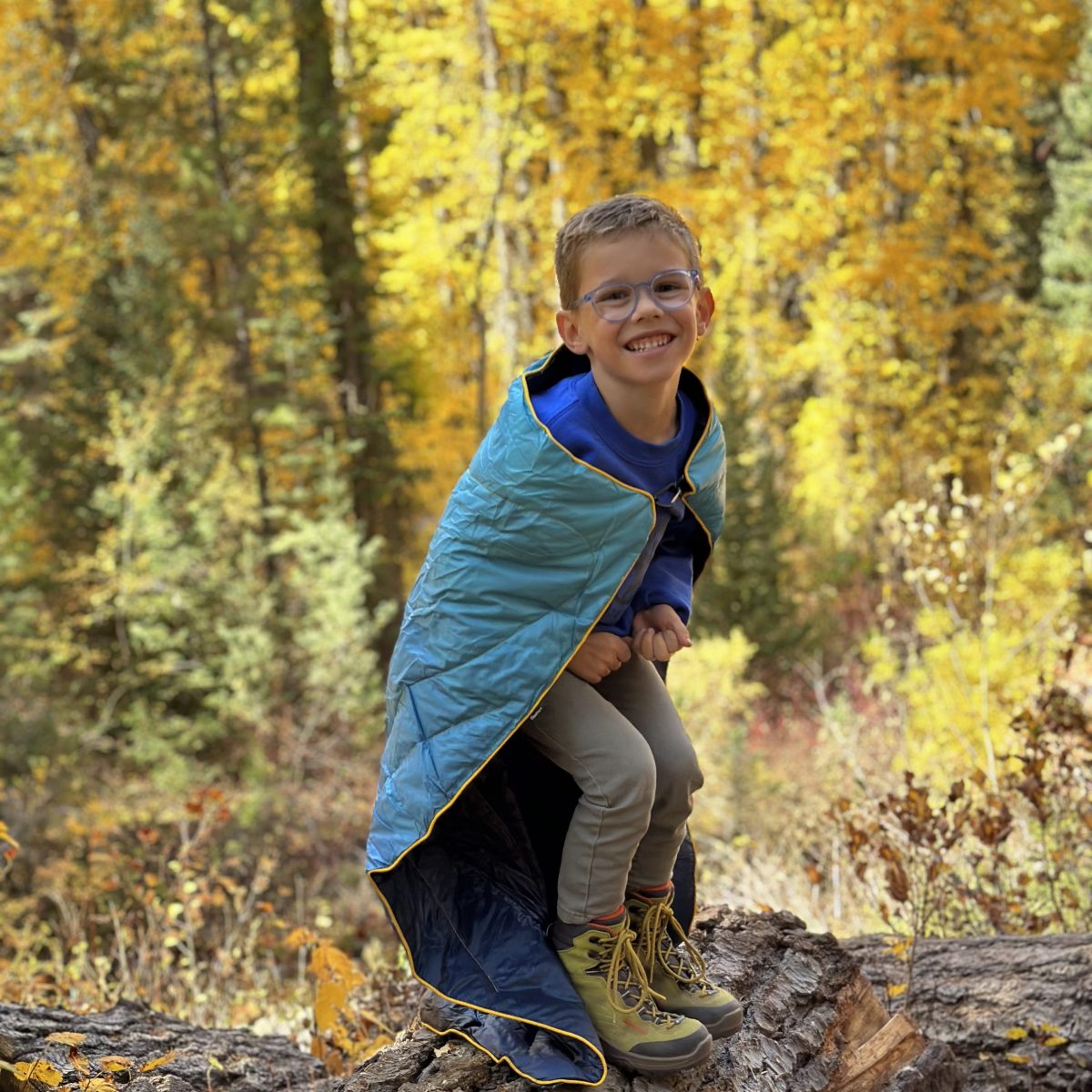 Young boy wrapped in a blanket poses on a log.